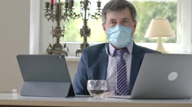 Takım elbiseli ve yüz maskeli ciddi bir beyaz adam portresi kabul ediyor ve kameraya katılmıyor. Kendine güvenen yakışıklı iş adamı Covid-19 tecridinde çevrimiçi sohbet ediyor. Uzak çalışma kavramı, serbest çalışma.