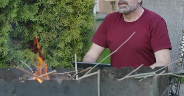 Rilassato uomo caucasico dai capelli grigi seduto di fronte alla griglia barbecue ardente e utilizzando tablet. Ritratto di bel ragazzo anziano che naviga su internet all'aria aperta. Stile di vita. Cinema 4k ProRes HQ . — Video Stock