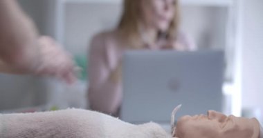 Erkek eller arka planda dizüstü bilgisayarla konuşan bulanık kadınlar gibi mankenlere harici kalp masajı yapıyor. İlk yardım pratiği yapan sağlık çalışanları. Sağlık hizmeti, ilaç. Sinema 4k ProRes Merkezi.