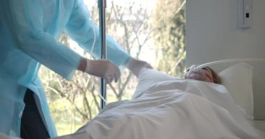 Erkek doktor, yorgun beyaz kadın için yastık ve battaniye ayarlıyor. Covid-19 teşhisi konmuş bir kadın hasta, hastane koğuşunda. Sağlık hizmeti, koronavirüs salgını. Sinema 4k ProRes Merkezi.