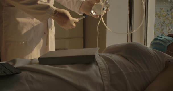 Tanınmayan bir doktor hastane koğuşunda düşürücü için ilaç karıştırıyor ve kadın hastayla konuşuyor. Tıbbi tedavi gören yüzü maskeli beyaz bir kadın. Sinema 4k ProRes Merkezi. — Stok video