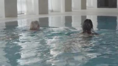 Tanımlanamayan genç beyaz kadınlar havuz kenarına yüzüyorlar. Sarışın ve esmer bayanların lüks spa otelinde hafta sonlarının tadını çıkardıkları arka manzara. Boş zaman, turizm, sağlık, rahatlama..