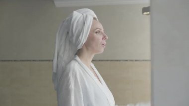 Rahat yetişkin bir kadın spa otelinde dinleniyor. Bornozlu, kendine güvenen sarışın kadının saç havlusunu düzelten portresi. Güzellik, rahatlık, rahatlama, yaşam tarzı..