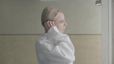 Beyaz bornozlu, kendine güvenen sarışın kadının kameraya dönüp gülümsemesinin yan görüntüsü. Hafta sonları spa otelinde eğlenen muhteşem beyaz kadın portresi. Boş zaman, güzellik, vücut bakımı.