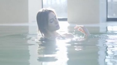 Güneşli havuzda poz veren güzel esmer kızın yakın plan portresi. Spa otelinde dinlenen güzel, genç, beyaz bir kadın. Yaşam tarzı, neşe, mutluluk, zenginlik, rahatlık.