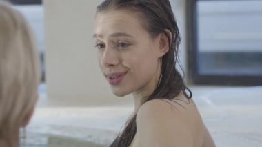 Pozitif esmer, kahverengi gözlü, sarışın, tanınmayan bir kadınla konuşan ve gülen bir kızın yan görüntüsü. Arkadaşınla yüzme havuzunda dinlenen büyüleyici mutlu müşterinin portresi. Yaşam biçimi.