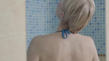 Havuzda yüzdükten sonra duş alan sarışın güzel bir kadın. Beyaz bir kadının kaplıcada cesedi yıkamasının arka görüntüsü. Boş zaman, yaşam tarzı, neşe, vücut bakımı.