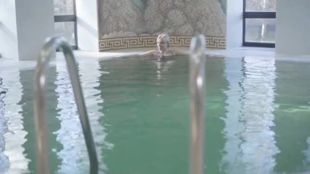 Mulher sorrindo loira cruzando a piscina, saindo e saindo. Retrato da senhora caucasiana positiva desfrutando da manhã no hotel spa. Lazer, turismo, beleza, alegria . — Vídeo de Stock