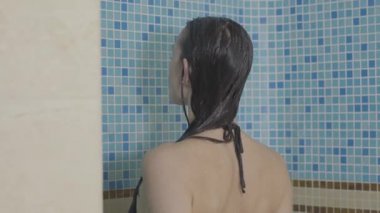Esmer, beyaz kadın duşta akan suyun altında duruyor. Yüzdükten sonra mayo giymiş genç bir kızın duş alışının arkası. Boş zaman, güzellik, vücut bakımı.
