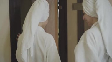 İki beyaz kadın lüks spa merkezindeki tuz terapi odasına giriyor. Kamera, bornozlu ve havluyla dinlenen yetişkin kadınları takip ediyor. Yaşam tarzı, lüks, güzellik, eğlence.