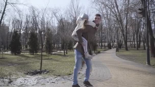 Joven y alegre padre dando vueltas a su pequeña hija en el parque de la ciudad. Retrato de un hombre y una chica felices descansando juntos al aire libre los fines de semana. Estilo de vida, alegría, felicidad, ocio . — Vídeos de Stock