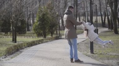 Güneşli bir günde, genç mutlu baba ve küçük kızın parkta eğlenirken geniş bir çekim. Beyaz bir adam kızı dışarı çıkarıp gülüyor. Neşe, mutluluk, yaşam tarzı, aile.