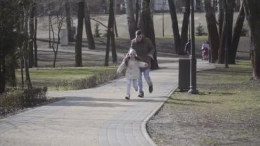 Neşeli genç beyaz adam güneşli parkta gülen küçük kızın peşinden koşuyor. Neşeli baba hafta sonları güzel kızıyla dışarıda oynuyor. Yaşam tarzı, aile eğlencesi, mutluluk, eğlence..