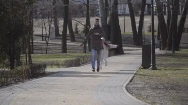 Neşeli küçük kız korkuyu taklit eden neşeli genç adamın peşinden koşuyor. Mutlu baba kız güneşli baharda ya da sonbahar parkında eğleniyorlar. Yaşam tarzı, neşe, eğlence, mutluluk..