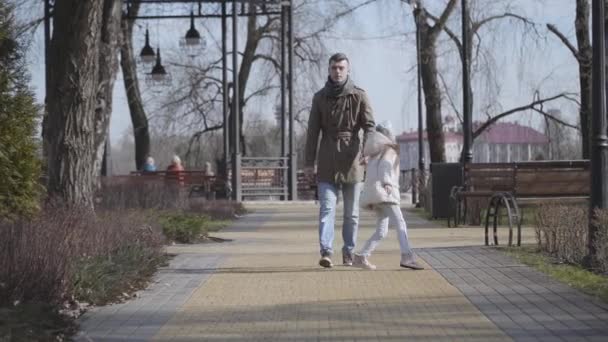 Active little Caucasian girl running around tired young father. Cheerful kid jumping and pulling mans hand. Daughter and parent strolling along the alley in autumn park. Joy, lifestyle, leisure. — Stock Video