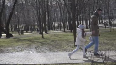 Küçük kızını okula gitmeye zorlayan beyaz bir babanın yan görüntüsü. Sonbaharı ya da bahar parkını geçen babasıyla okula yürüyen gönülsüz, sevimli kız öğrenci. Yaşam tarzı, eğitim, aile.