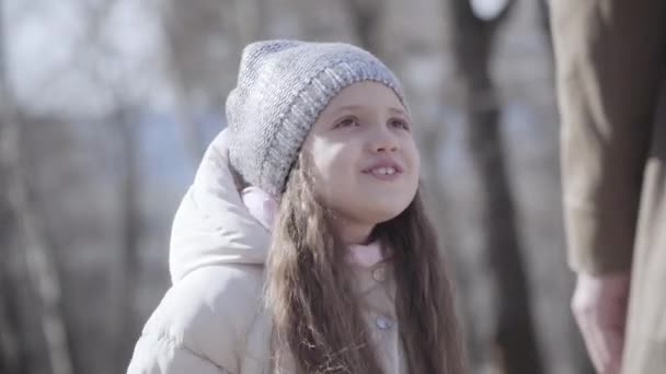 Close-up portrait of mischievous little girl gesturing and rubbing eyes outdoors. Disobedient daughter talking to unrecognizable parent in spring or autumn park. Lifestyle. — Stock Video