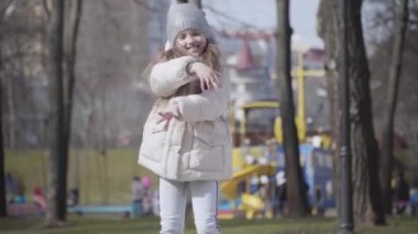 Sonbahar parkında dans eden neşeli küçük bir kızın orta sahnesi. Güneşli bir sonbahar gününde neşeli, güzel bir çocuğun atlama ve el kol hareketi portresi. Boş zaman, eğlence, eğlence, yaşam tarzı.
