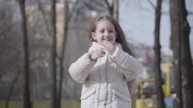 Esmer, beyaz, saçları kıvırcık, parkta tanınmayan biri gibi poz veren bir kızın portresi. Güzel bir çocuğun bahar ya da sonbahar gününün tadını çıkarırken orta pozu. Neşe, yaşam tarzı.