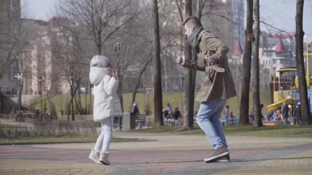 Divertida danza de alegre padre e hija caucásicos en el parque de primavera u otoño. Joven hombre feliz y niña linda bailando y divirtiéndose al aire libre los fines de semana. Ocio, estilo de vida, alegría . — Vídeo de stock