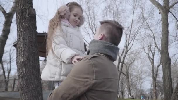 Niña alegre hablando con el joven padre en el parque y sonriendo. Retrato de un niño caucásico de pelo rizado morena disfrutando del tiempo con sus padres al aire libre en el día de primavera. Amor, familia, infancia, unidad . — Vídeos de Stock