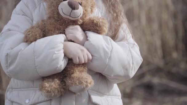 Primer plano de una niña irreconocible apretando un osito de peluche en las manos. Niño caucásico asustado perdido al aire libre. Problemas sociales, secuestro, miedo, riesgo . — Vídeo de stock