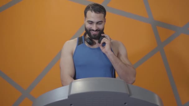 Vista frontal de deportista guapo confiado que comienza el entrenamiento en la cinta de correr. Retrato del joven hombre de Oriente Medio encendiendo el equipo en el gimnasio y trotando. Deporte, entrenamiento, masculinidad, atletismo . — Vídeo de stock