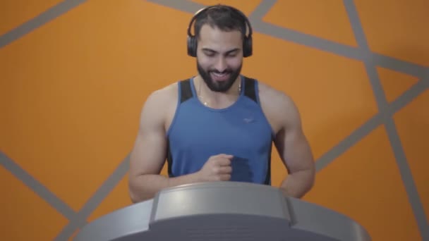 Retrato de joven deportista en auriculares trotando en la cinta de correr. Guapo hombre de Oriente Medio fuerte entrenando en el gimnasio. Vida sana, deporte, entrenamiento, atletismo . — Vídeo de stock