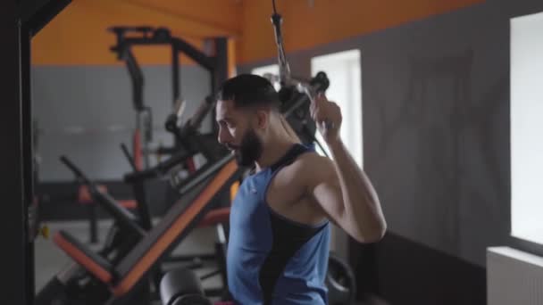 Boční pohled na svalnatého sportovce ze Středního východu, který používá stroj na stahování ramen v tělocvičně. Silný pohledný muž trénuje svaly na zádech. Sport, cvičení, čas, vytrvalost, životní styl. — Stock video
