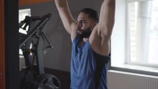 Mladý sebevědomý sportovec trénuje svaly pomocí stroje. Soustředěný muž ze Středního východu cvičí v tělocvičně. Sport, životní styl, vytrvalost, cvičení.