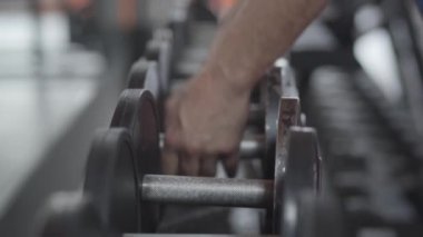 Spor salonunda erkek ellerinin ağır dambıllar almasına yakın çekim. Spor kulübünde ağırlık kaldırmak için ekipman kullanan tanınmayan yetişkin bir sporcu. Spor, spor, sağlıklı yaşam tarzı, spor.