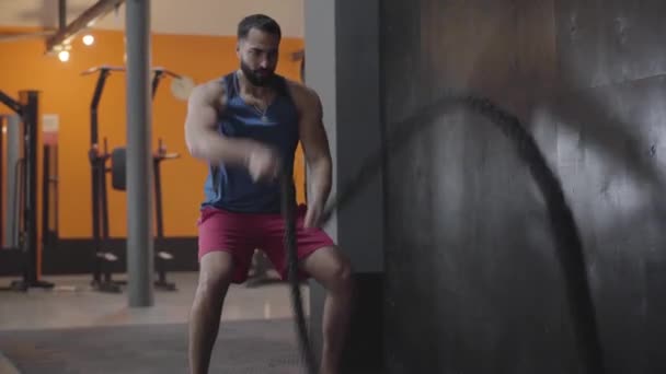 Ισχυρή μυώδης αθλητής κάνει crossfit άσκηση στο γυμναστήριο. Ευρεία βολή ενός όμορφου άντρα της Μέσης Ανατολής που χρησιμοποιεί σχοινιά για εκπαίδευση αντοχής. Αθλητισμός, τρόπος ζωής, υγεία, προπόνηση. — Αρχείο Βίντεο