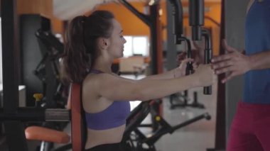 Bilinmeyen kişisel eğitmenin yardımıyla el kaslarını çalıştıran konsantre beyaz kadın görüntüsü. Spor salonundaki sporcu kızın antrenmanı. Egzersiz, spor, sağlıklı yaşam tarzı..