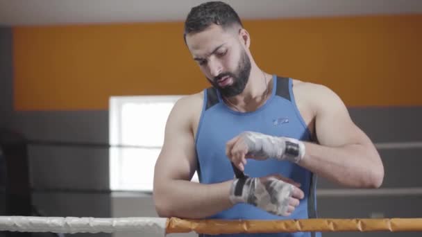 Deportista confiado envolviendo vendas de boxeo en las palmas. Retrato del guapo boxeador de Oriente Medio preparándose para el entrenamiento de boxeo en el gimnasio. Deportes, estilo de vida, resistencia, bienestar . — Vídeo de stock