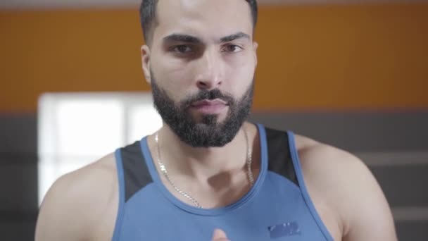 Primer plano del boxeador de ojos marrones de Oriente Medio apuntando a cámara y espalda. Joven deportista guapo confiado posando en el gimnasio. Deporte, salud, resistencia, estilo de vida . — Vídeo de stock