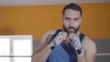 Kameraya bakan yakışıklı boksör boksörlerin yakın çekimi. Orta Doğulu genç bir adamın spor salonunda havadan kaçarken ve yumruk atarken portresi. Spor, özgüven, yaşam tarzı, antrenman, spor. Ön görünüm.