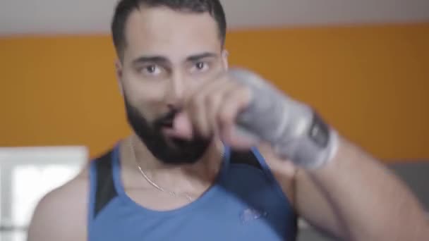 Un boxeur masculin confiant qui frappe de l'air, la caméra remonte. Portrait d'un jeune homme aux yeux bruns du Moyen-Orient boxant dans un gymnase. Caméra en direct, vue de face. Sport, mode de vie, force . — Video