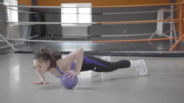 Mince jeune femme caucasienne poussant vers le haut en utilisant la balle dans la salle de gym. Portrait d'une sportive forte et confiante faisant de l'exercice dans un club sportif. Concept de sport, mode de vie sain, entraînement, endurance . — Video
