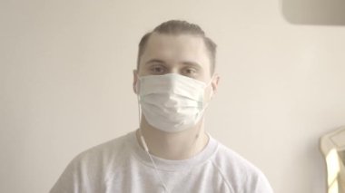 Yüz maskeli genç adamın yakın plan portresi meslektaşlarını veya arkadaşlarını internette selamlıyor. Beyaz tenli esmer adam video konferansı için poz veriyor. Covid-19, uzaktan kumanda. S-seyir defteri 2, QuickTime ProRes 422 HQ.
