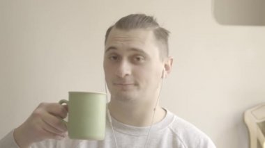 Çay ya da kahve içen ve kamerayla şakırdayan gülümseyen genç adamın portresi. Covid-19 'daki izole edilmiş esmer, beyaz adamın yakın çekimi. S-seyir defteri 2, QuickTime ProRes 422 HQ.