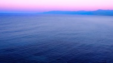 Akdeniz 'in sakin mavi suları. Tepeler, dağlar ve arka planda pembe günbatımı. Gün batımında Kıbrıs 'ın deniz manzarası çok geniş. Doğa, manzara, yaz tatili, turizm.