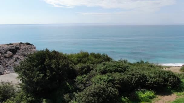 Kamera se zvedá a ukazuje klidné mořské pobřeží a osamělé červené auto projíždějící kolem silnice. Letecký pohled na pobřeží Kypru ve Středozemním moři. Příroda, moře, klid, slunečný den v turistickém letovisku. — Stock video