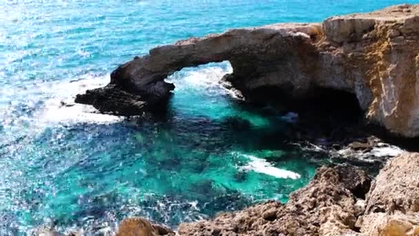 Rocce marine marroni con acqua blu e turchese intorno. Onde che schizzano e si schiantano con schiuma sulle pietre. Bellezza del Mar Mediterraneo. Cipro località nella giornata di sole in estate . — Video Stock