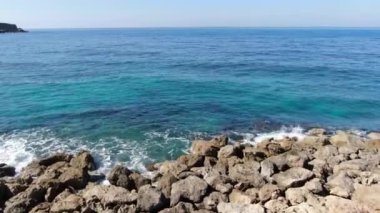 Kamera kayalık sahilden turkuaz mavi dalgalar boyunca ilerler. Muhteşem Kıbrıs doğasının deniz manzarası. Akdeniz 'de güneşli bir yaz günü. Doğa, güzellik.