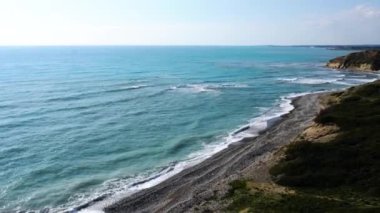 Kıbrıs 'ın deniz manzarası. Mavi, sakin Akdeniz dalgaları ıslak çakıl taşı plajında yuvarlanıyor. Gün batımında deniz kıyısında. Doğa, manzara, drone görünümü, güzellik.