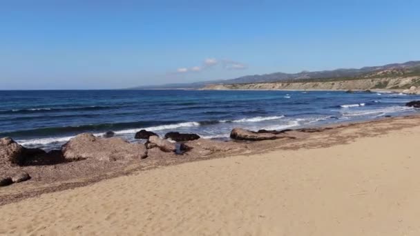 Αμμώδης παραλία της Μεσογείου Θάλασσας με σκούρα μπλε κύματα που πιτσιλίζουν στις ακτίνες του ήλιου. Ευρεία φωτογραφία του τουριστικού θέρετρου της Κύπρου την ηλιόλουστη μέρα. Τουρισμός, διακοπές, φύση, ομορφιά, θαλασσογραφία. — Αρχείο Βίντεο