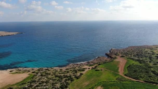 Eindeloze Middellandse Zee in de zon. Camera beweegt weg van rustig water naar groene vallei of weide rond. Luchtfoto van het prachtige Cyprus natuur op zonnige zomerdag. Toerisme, landschap, landschap. — Stockvideo