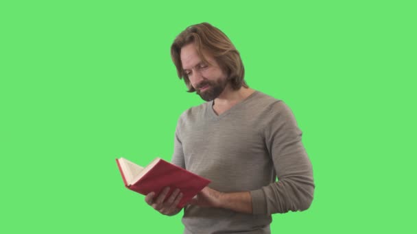 똑똑 한 백인 남자빨간 커버로 책을 마무리하고 카메라로 웃고 있어요. 초록색 배경에 성숙 한 수염 남자의 초상화. 크로마키, 녹색 화면, 지능, 독서, 문학. — 비디오