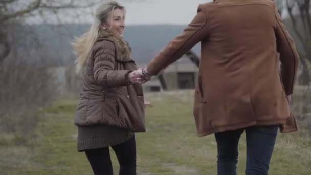 Couple caucasien adulte joyeux courant à l'extérieur en se tenant la main. Joyeux homme brune étreignant et filant femme blonde souriante. Joie, plaisir, loisirs, rencontres, amour . — Video
