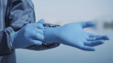 Mavi koruyucu eldiven takan insan elinin yakın çekimi. Antiviral takım elbiseli tanınmayan bir işçi halka açık bir yeri dezenfekte etmeye hazırlanıyor. Covid-19, hava kirliliği, küresel tehlike.